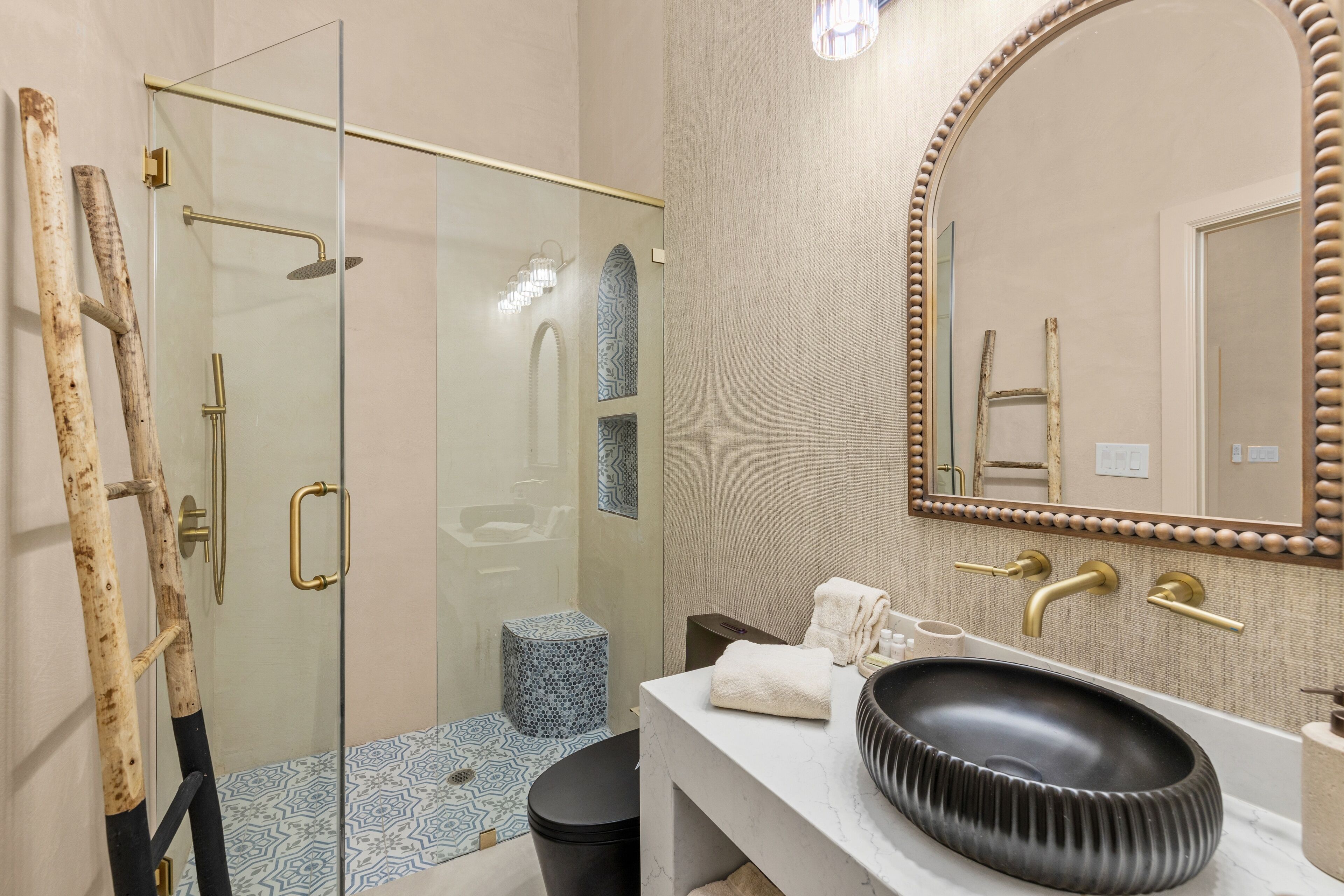A modern bathroom with a glass-enclosed shower, a vanity with a black sink, and a large mirror with a decorative frame.