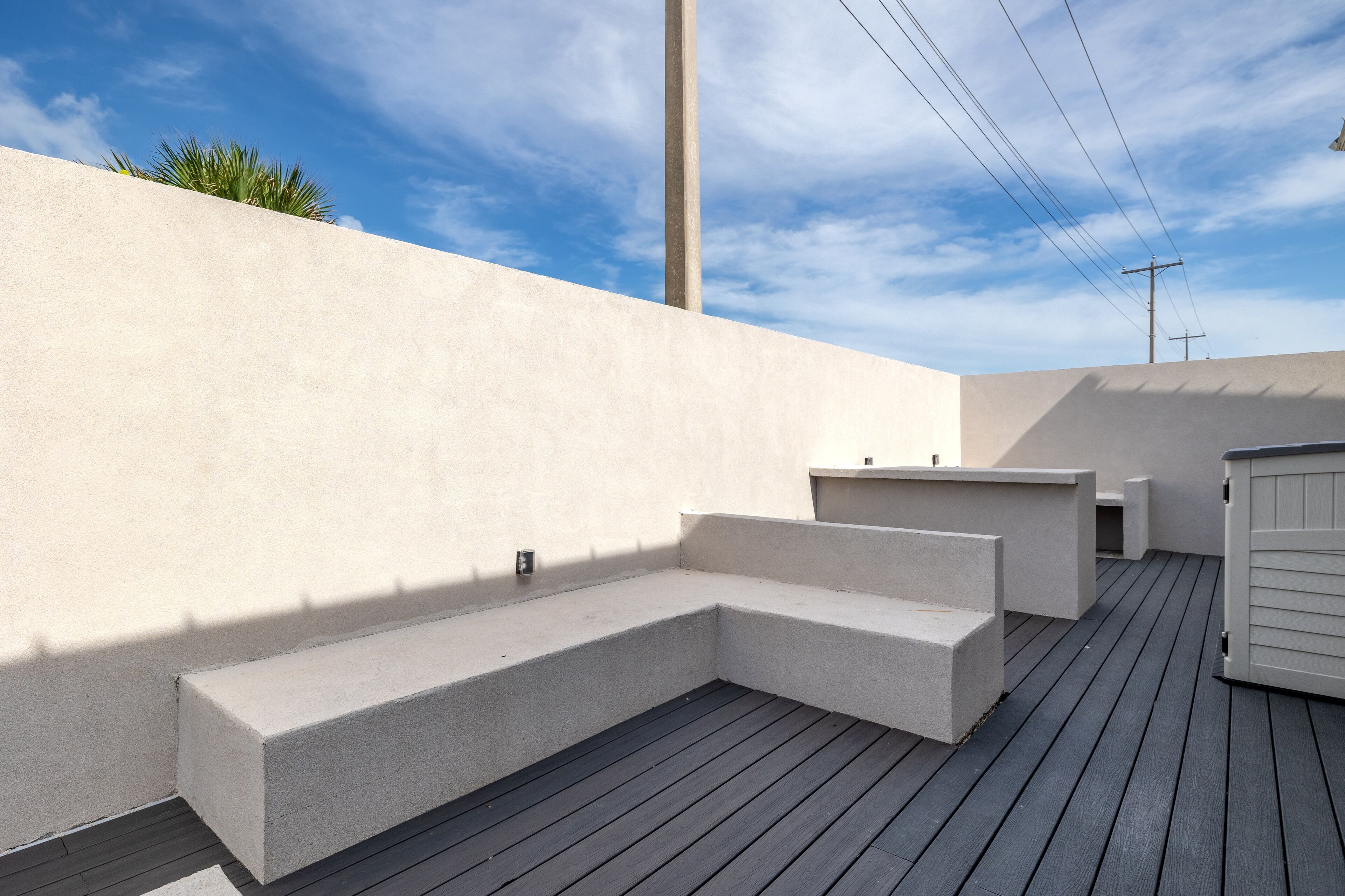 An outdoor deck with concrete steps and a wooden floor, surrounded by a white wall and a clear blue sky.