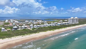 An aerial view of a coastal resort with multiple buildings, a beachfront, and a clear sky.