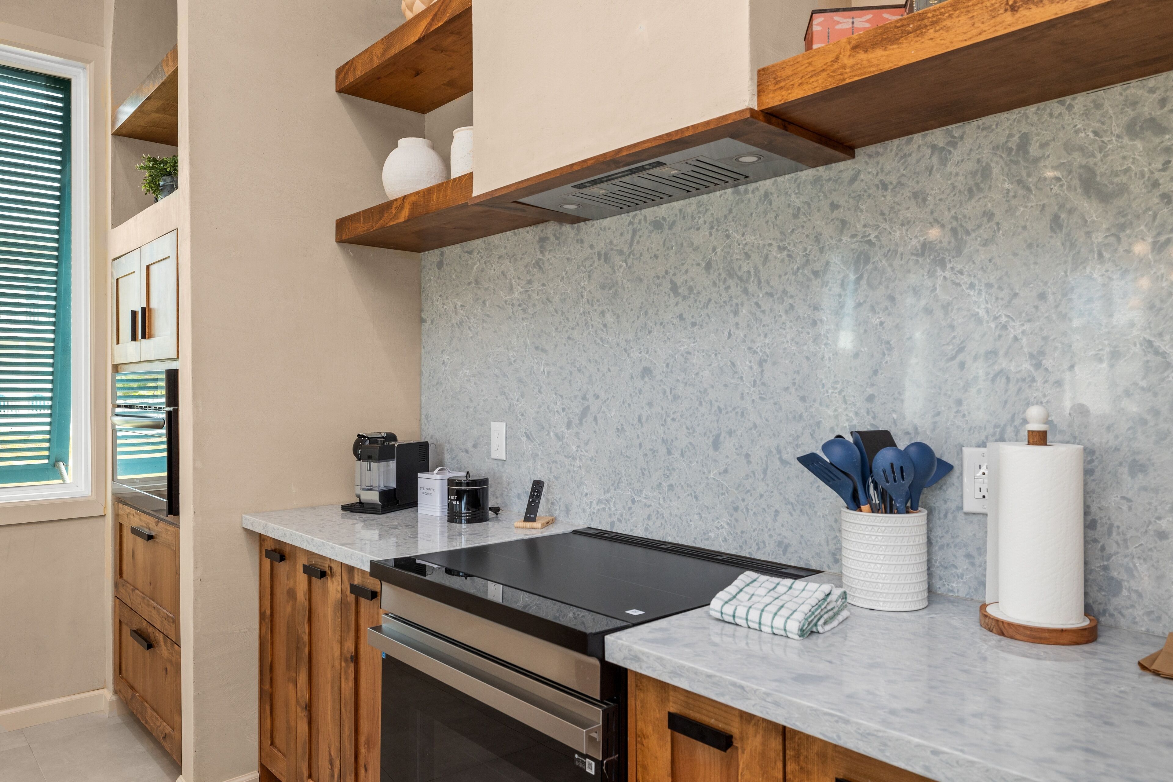 A modern kitchen with a granite countertop, stainless steel appliances, wooden cabinets, and a built-in stove.