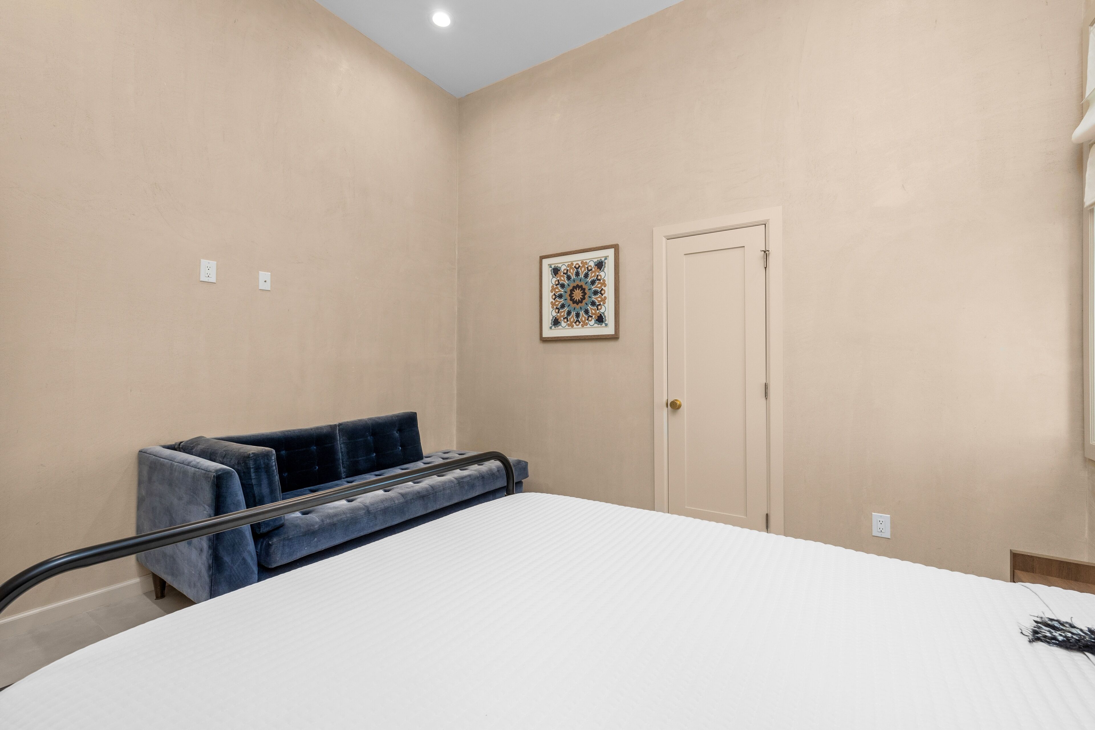 Un dormitorio con cama, sofá azul, una puerta y un cuadro colgado en la pared.