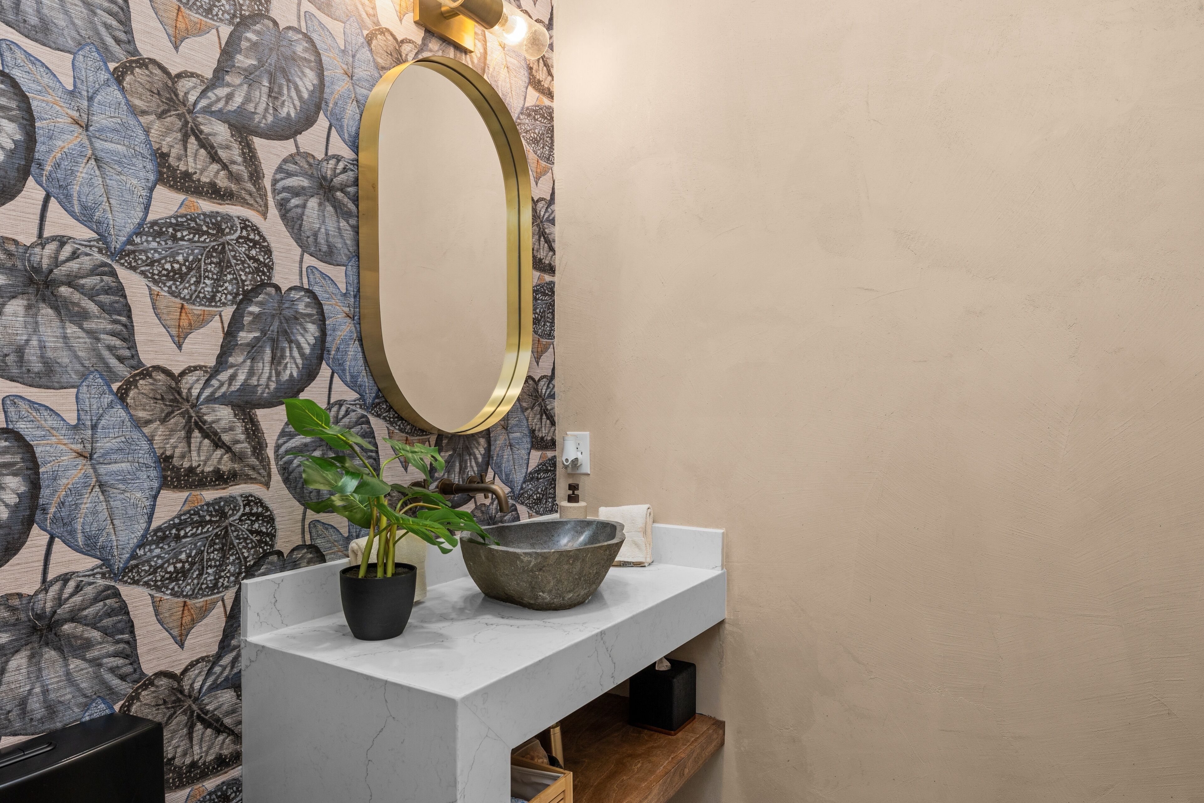 A bathroom with a marble sink, a large mirror, a potted plant, and a decorative wall with leaf patterns.