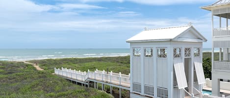 A beach house with a wooden deck and a small tower structure.