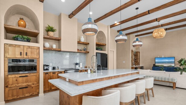 A modern kitchen with wooden cabinets, a marble island, and pendant lighting.
