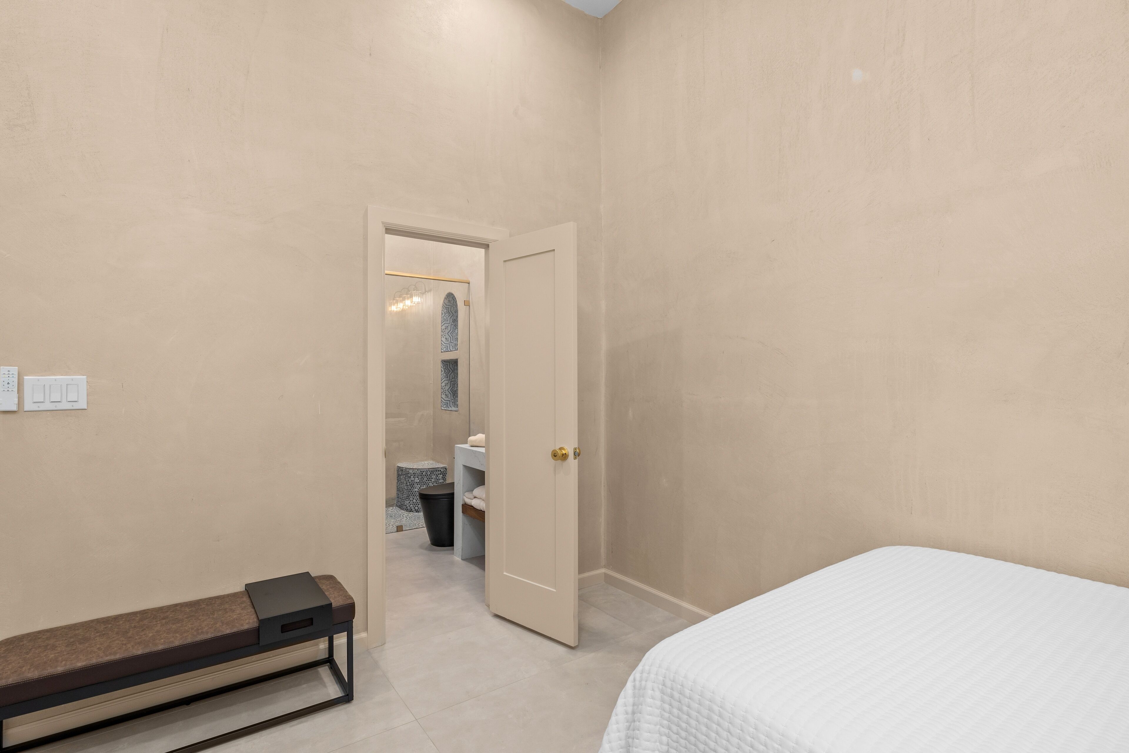 A bedroom with a bed, a bench, and a door leading to a bathroom.