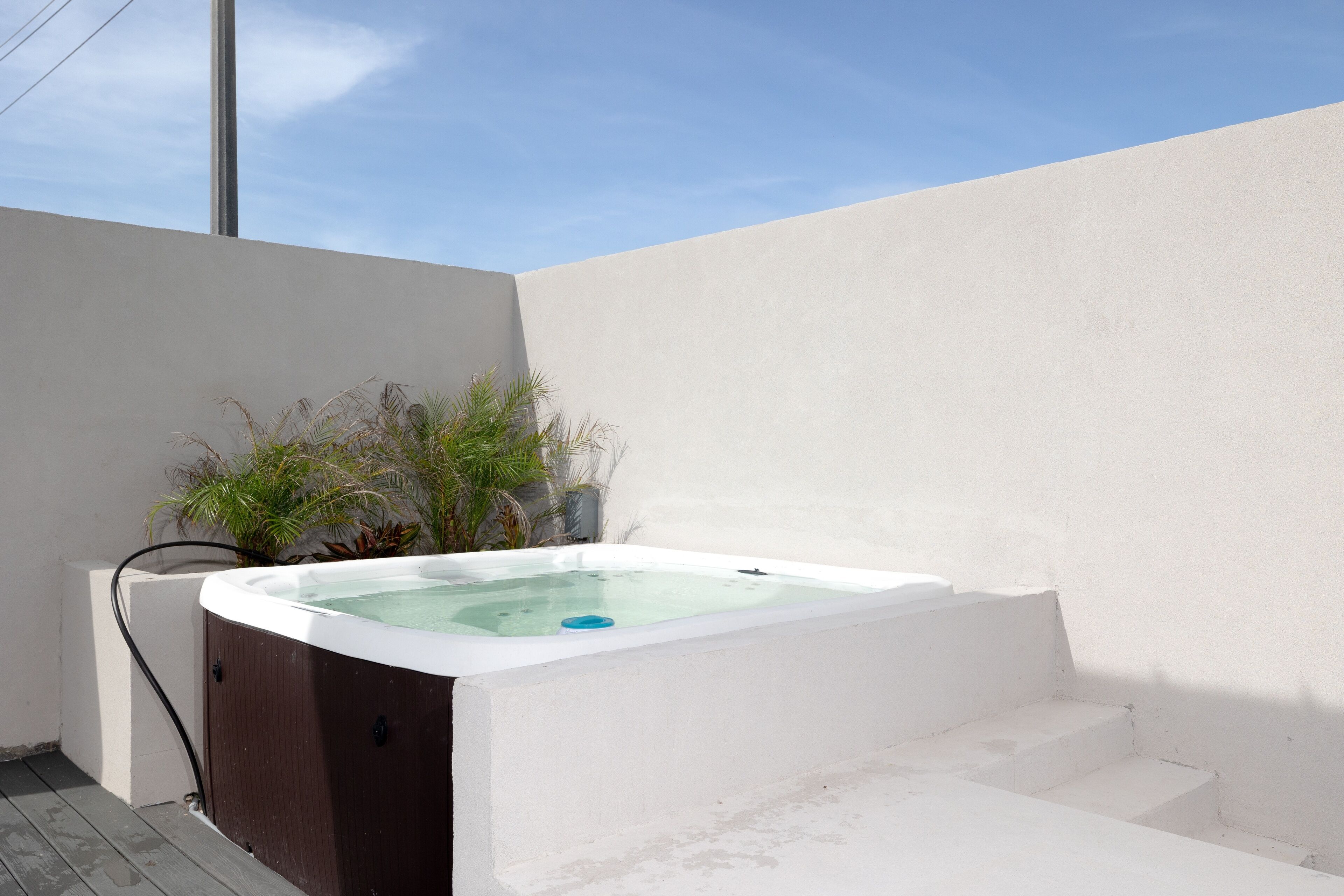 A hot tub with a wooden exterior, surrounded by a white wall and steps leading up to it.