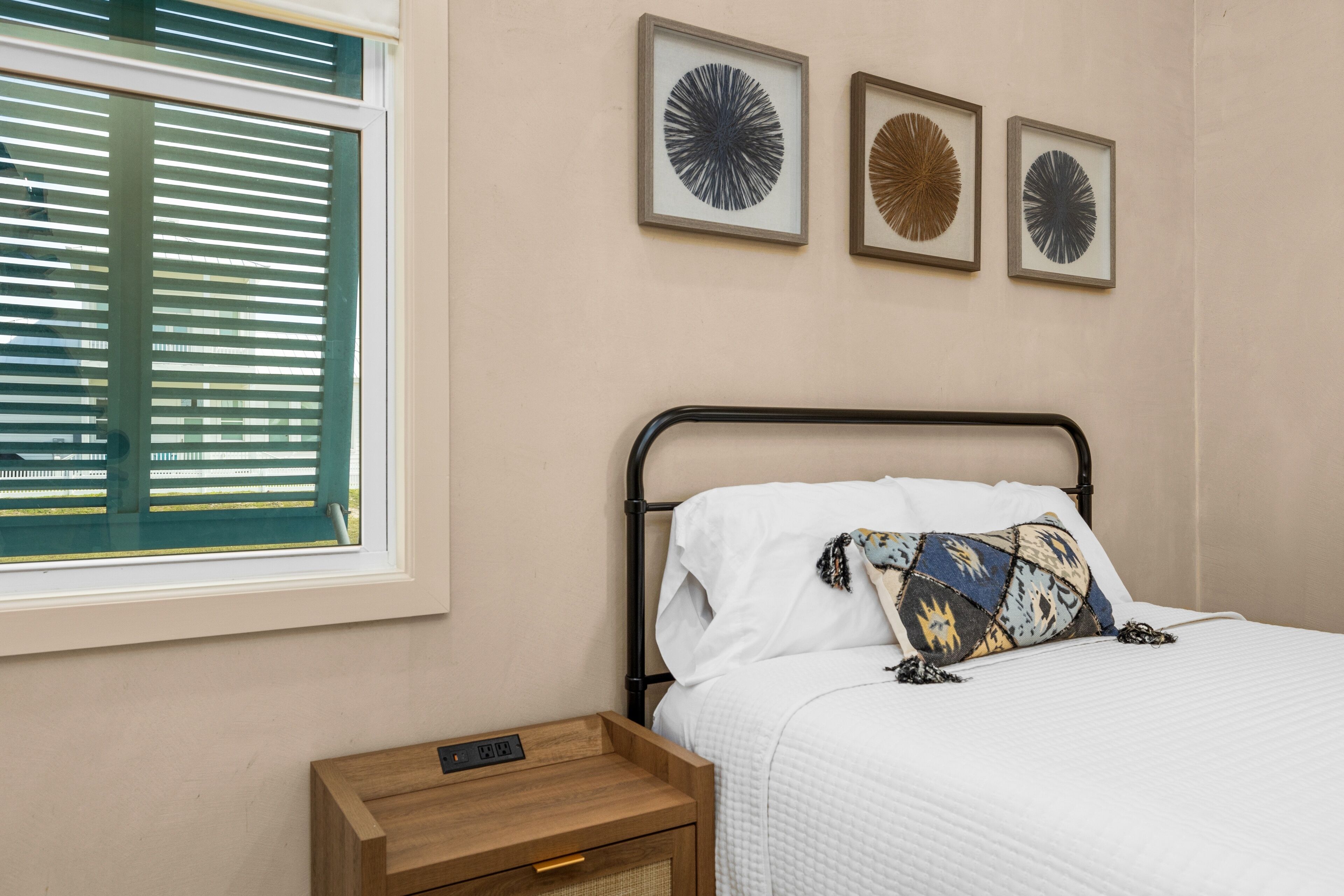 Un dormitorio con una cama, una mesita de noche con un reloj y tres cuadros enmarcados en la pared.