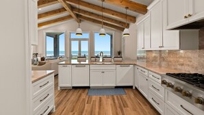 Eine moderne Küche mit weißen Schränken, einer Holzbalkendecke und Blick ins Freie.