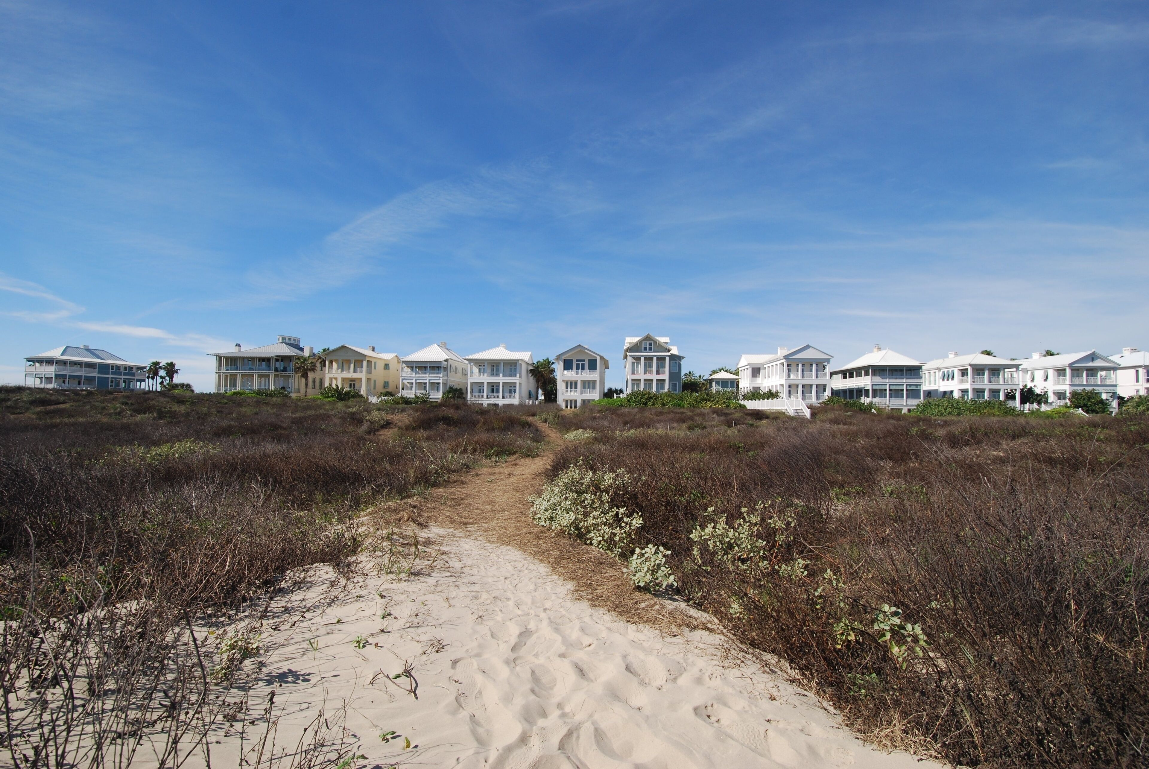 Une propriété située en bord de mer, avec un sentier sablonneux menant à une rangée de maisons blanches.