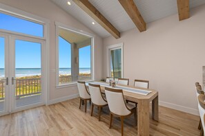 Ein Essbereich mit Holztisch und -stühlen, großen Fenstern mit Meerblick und einer Decke mit freiliegenden Balken.