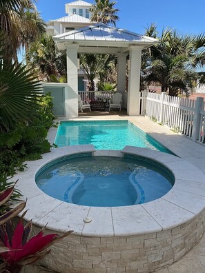 Ein Swimmingpool mit Whirlpool, umgeben von einem weißen Zaun, Palmen und einem überdachten Sitzbereich.