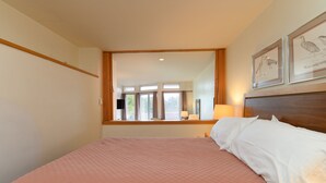Une chambre avec un grand lit, une fenêtre donnant sur un beau paysage et des œuvres d’art encadrées accrochées au mur.