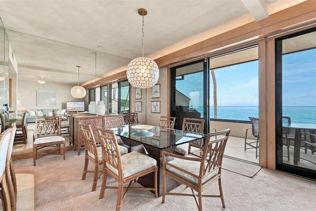 Uma área de jantar moderna com mesa de vidro e cadeiras de vime, com vista para o oceano.