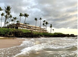 A beachfront hotel with a multi-story structure, palm trees, and a rocky shoreline. - Makena Surf, #f-206 2 Bedroom Condo (Kihei)