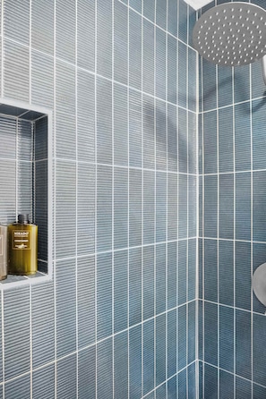 A bathroom with a blue tiled wall and a showerhead. There is a shelf with two bottles. - Steps to Beach Patio Fire Pit Tropical Oasis (St. Augustine)