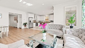 A modern living room with a glass coffee table, a beige sofa, and a dining area with a white table and chairs. - Stylish 3BR Irvine Oasis Family Friendly w Garage (Tustin)