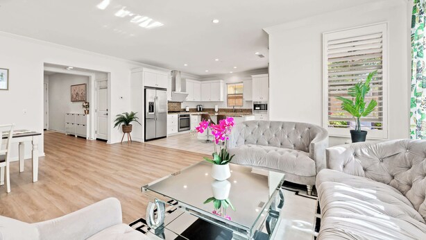 Una sala de estar moderna con una mesa de centro de vidrio, un sofá color beige y un comedor con una mesa y sillas blancas.
