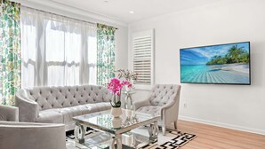 Un salón moderno con un sofá capitonado, una mesa de centro de cristal y una escena de playa tropical en la pared.