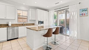 Cocina moderna con armarios blancos, encimera de granito, electrodomésticos de acero inoxidable y una zona de bar con taburetes.