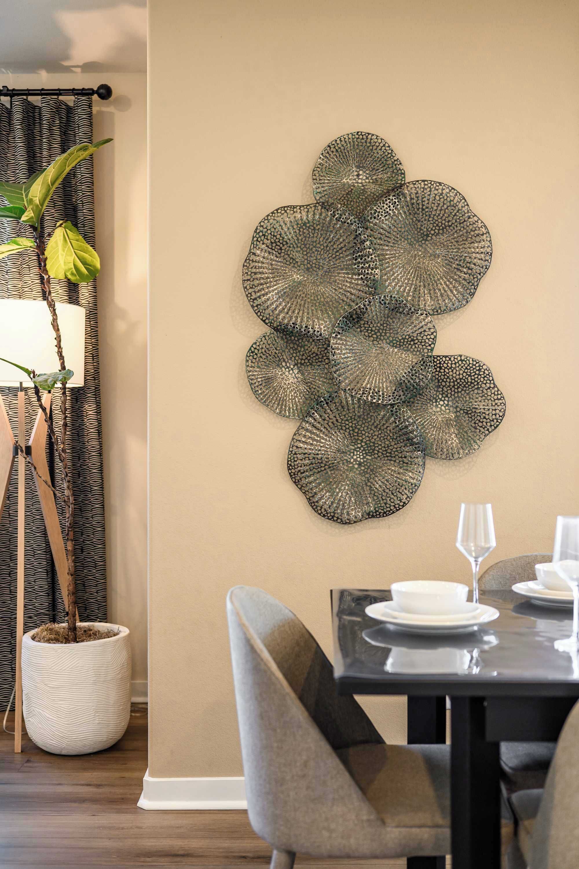 Zona pranzo con tavolo apparecchiato per due, un elemento decorativo a parete e una pianta in vaso.