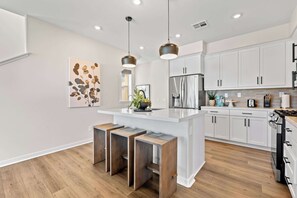 A modern kitchen with white cabinets, a central island with stools, pendant lighting, and a stainless steel refrigerator. - Designer 3BR El Monte Retreat Near Dtla Pasadena (El Monte)