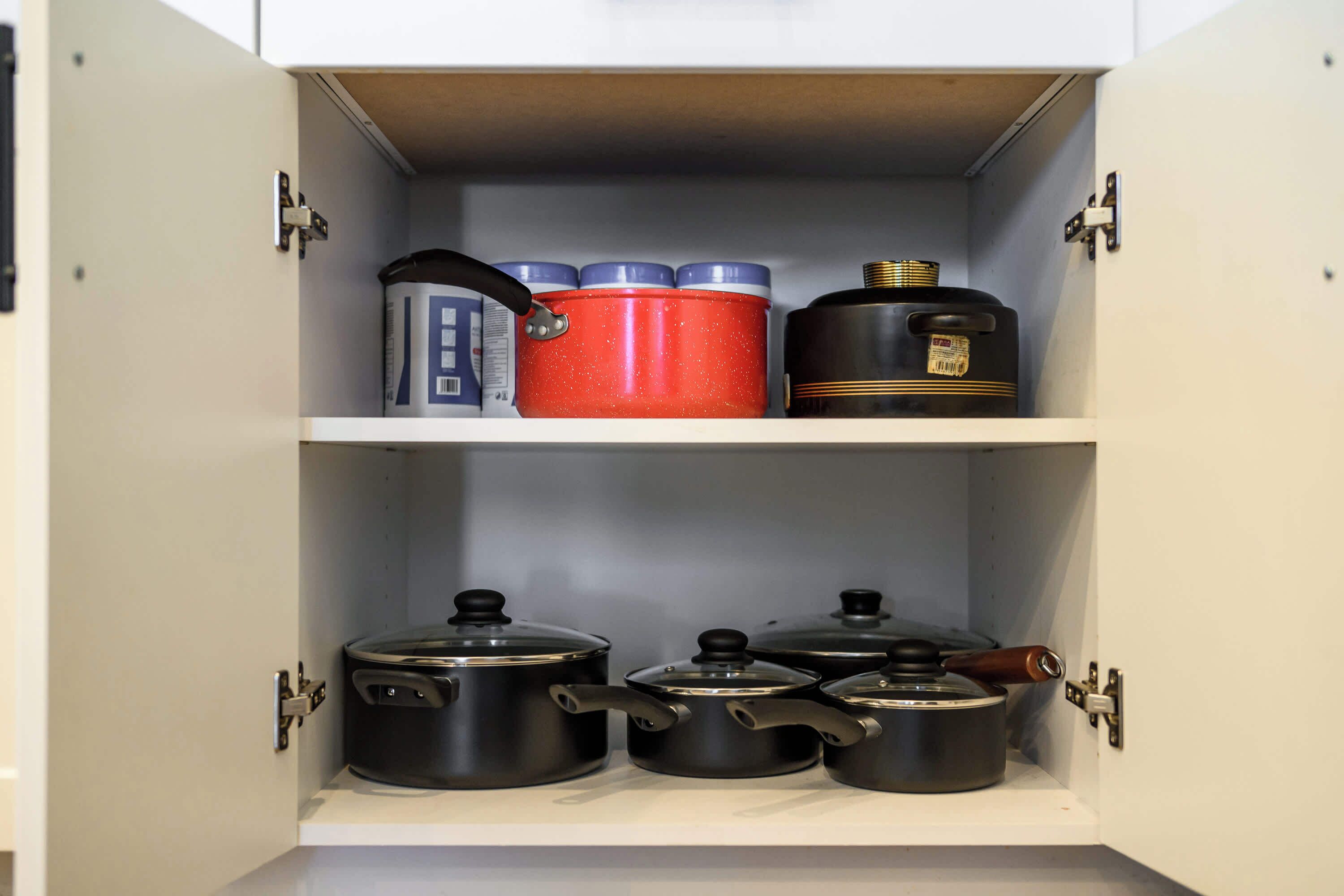 A kitchen cabinet with three pots on the top shelf and three pots on the bottom shelf.