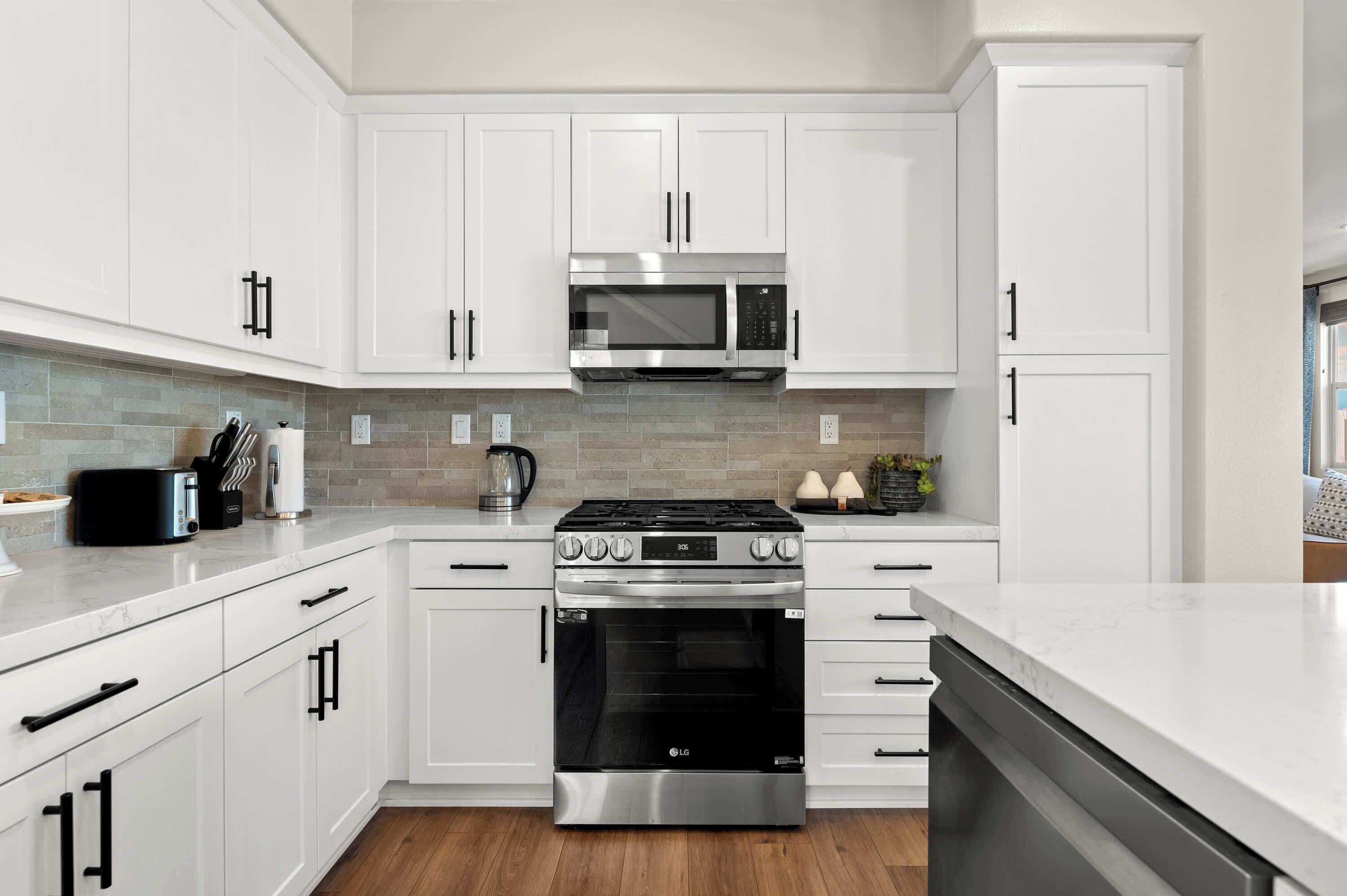Une cuisine moderne avec des meubles blancs, une cuisinière en acier inoxydable, un four et un four à micro-ondes.