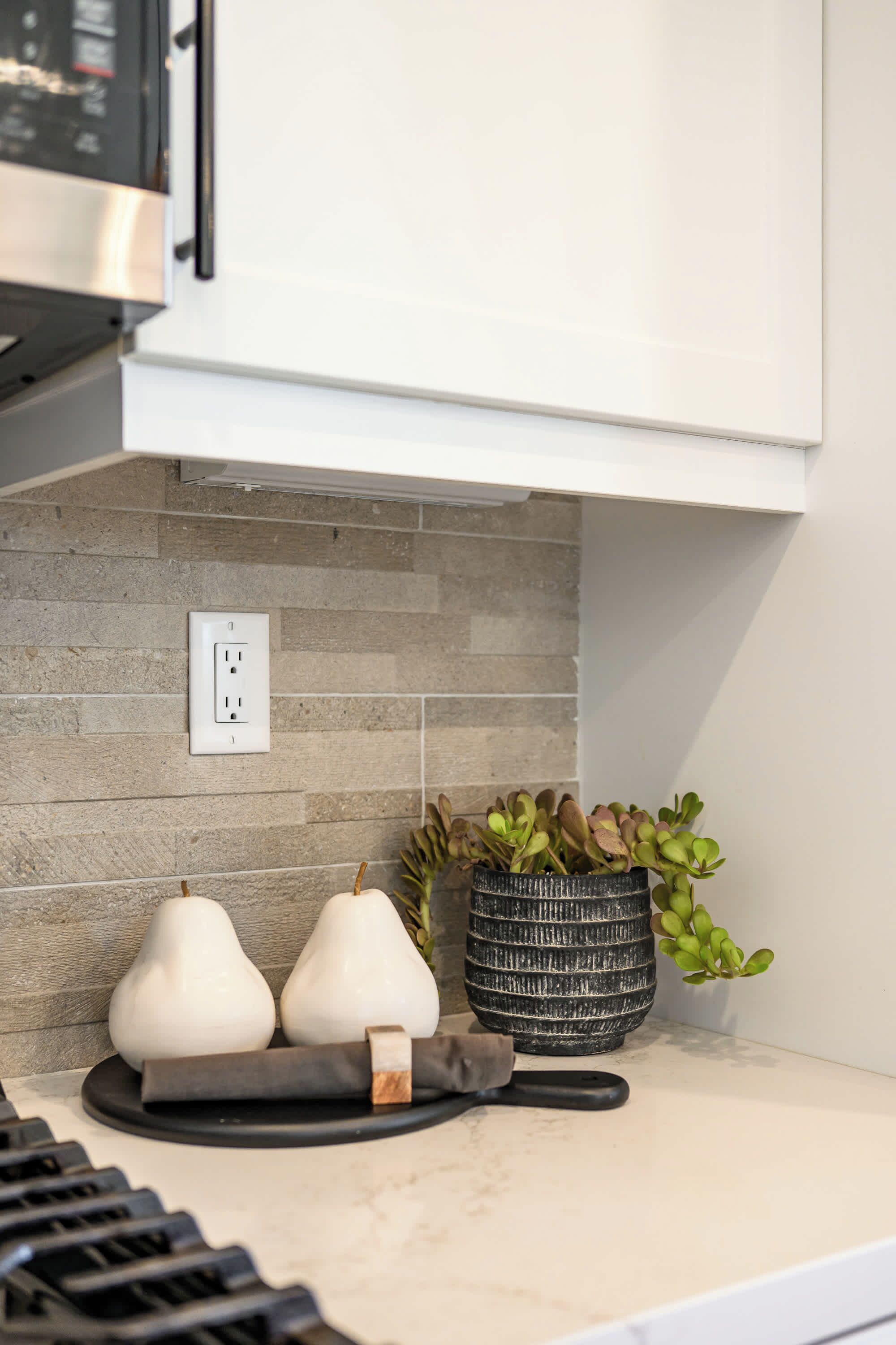 Una encimera de cocina con diseño moderno, que incluye una planta en maceta, dos jarrones decorativos y una tabla de cortar.