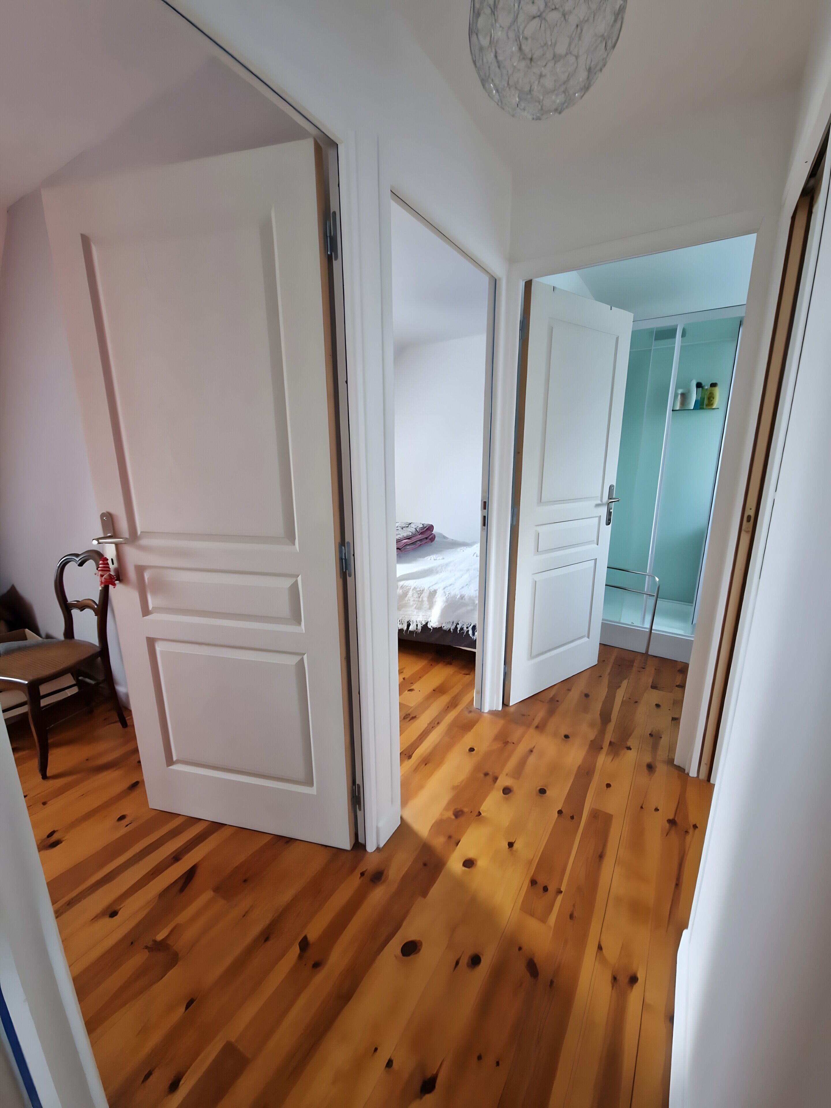 Ein Flur mit Holzboden, weißen Türen und einem Bett mit weißer Decke.