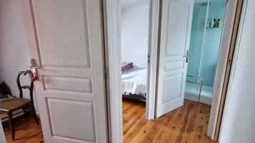 Ein Flur mit Holzboden, weißen Türen und einem Bett mit weißer Decke.