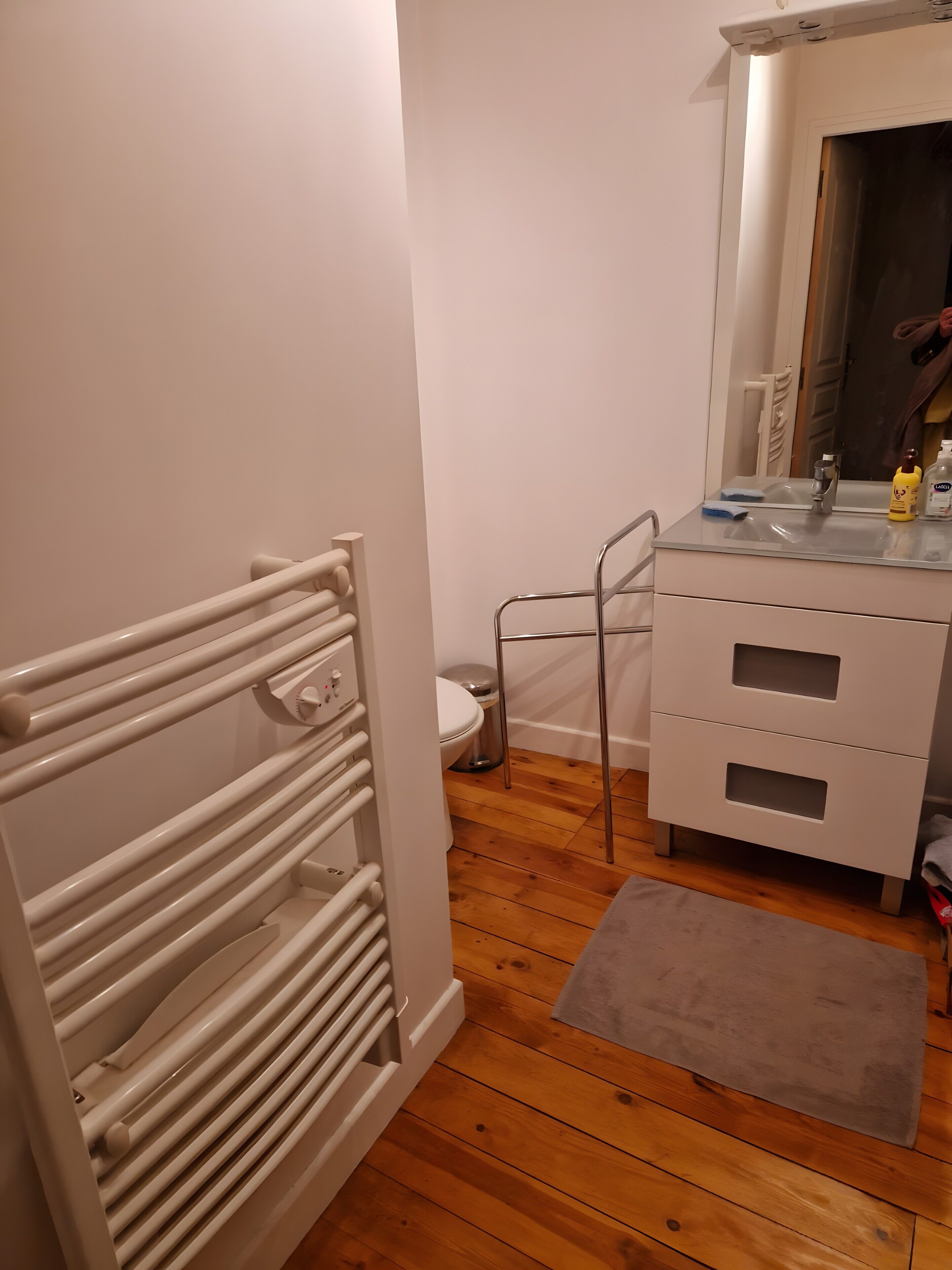 Casa de banho com radiador branco, sanita, lavatório com espelho e armário.