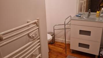 Casa de banho com radiador branco, sanita, lavatório com espelho e armário.