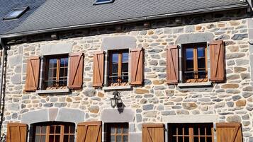 Un bâtiment en pierre doté de nombreuses fenêtres et de volets, d’une porte et d’une petite table à l’extérieur.