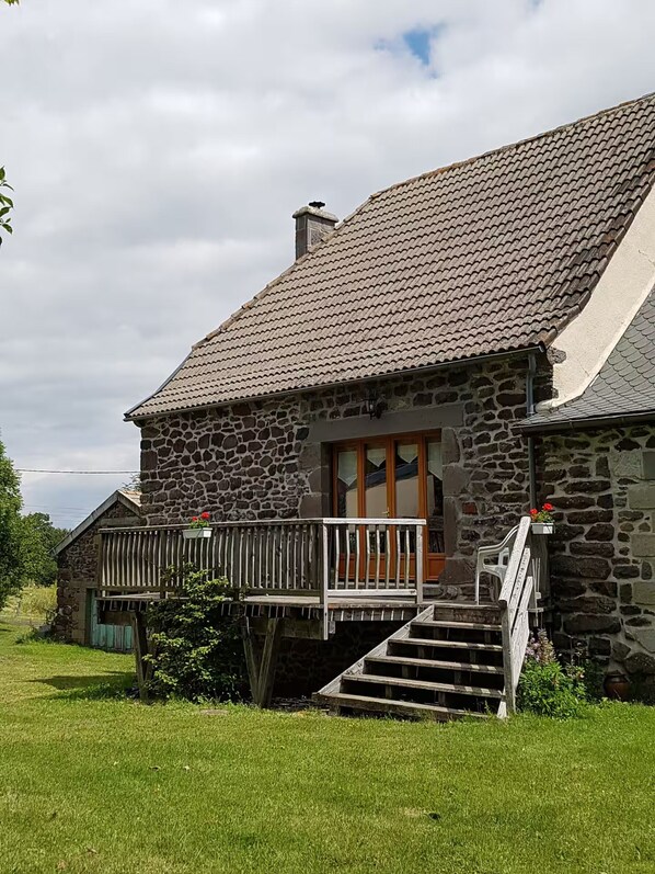 Ein Haus aus Stein mit Ziegeldach und einer Holzveranda, mit einer Treppe, die zum Eingang führt.