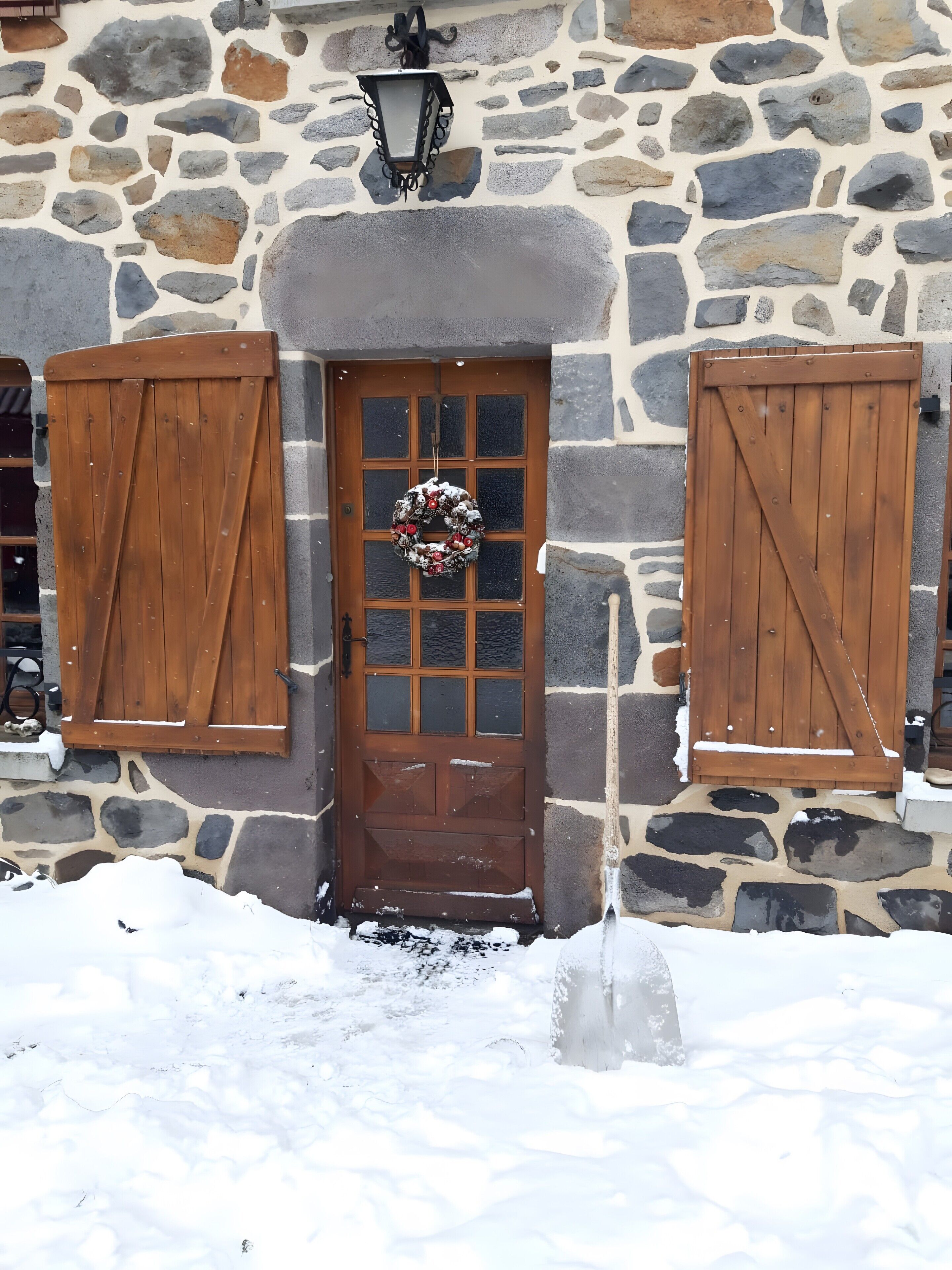 Un bâtiment en pierre avec une porte en bois, une couronne et un sol recouvert de neige.