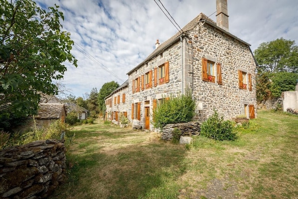 A stone building with multiple windows and a chimney, surrounded by a grassy area and stone walls.