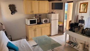 A compact living space with a kitchenette, a glass-top table, and a sofa with cushions.