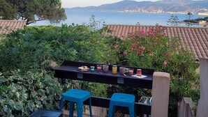 A terrace with a table set for a meal, overlooking a coastal landscape with mountains and a body of water.