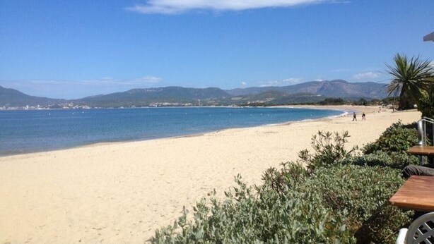 A beach with a clear sky, distant mountains, and a few people walking.