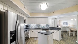 A modern kitchen with stainless steel appliances, white cabinetry, and a central island. - Windward Pointe 1102 by Liquid Life (Orange Beach)