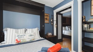 Un dormitorio con una cama, un reposapiés azul, una mesita de noche y una estantería.