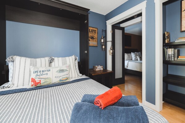 Un dormitorio con una cama, un reposapiés azul, una mesita de noche y una estantería.