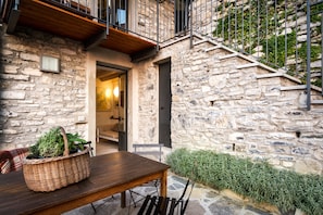 Un edificio in pietra con un tavolo e sedie in legno, un cesto di vimini con piante e una scala che conduce a un piano superiore.