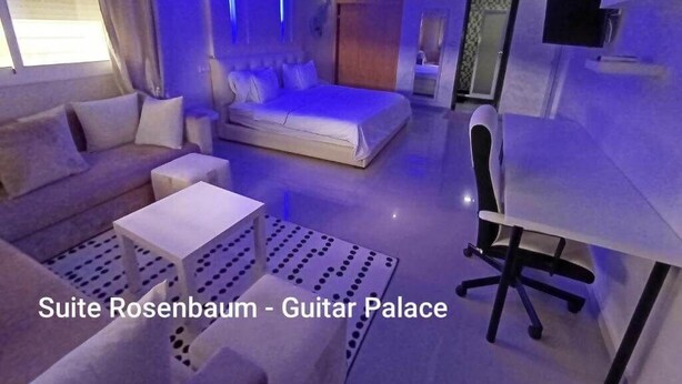 A modern suite with a bed, sofa, and desk, featuring a unique blue lighting design. - Guitar Palace (Bni Quolla)