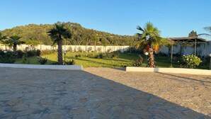 A courtyard with stone flooring, palm trees, and a grassy area with flowers. - Guitar Palace (Bni Quolla)