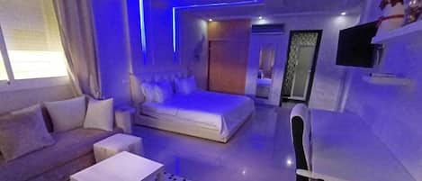 A modern suite with a bed, sofa, and desk, featuring a unique blue lighting design.