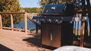 Un jacuzzi en una terraza de madera, con una parrilla y una valla de madera al fondo.