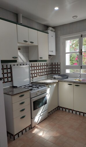 A kitchen with white cabinets, a gas stove, an oven, a window with a view of greenery, and a tiled backsplash. - Apartment in Yasmine Hammamet  Near Beach & Marina (Yasmine Hammamet)