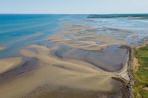 Vue aérienne d’une zone côtière avec des bancs de sable et une étroite bande de terre bordée d’une côte rocheuse.