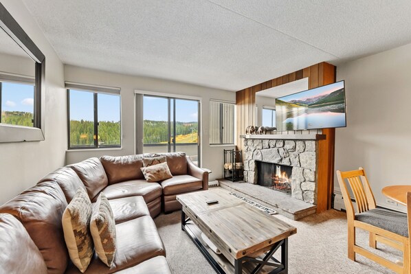 A modern living room with a leather sectional sofa, a stone fireplace, a wooden coffee table, and a television mounted on the wall. - Best Of Summit 2025 Winner for Best Lodging Hotel! Premium Slopeside Escape at B (Breckenridge)